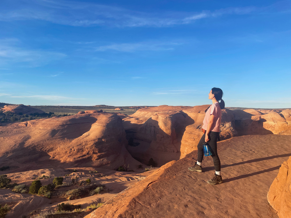 Woman standing on a narrow sandstone trail looking at the landscape of tall sandstone fins. 