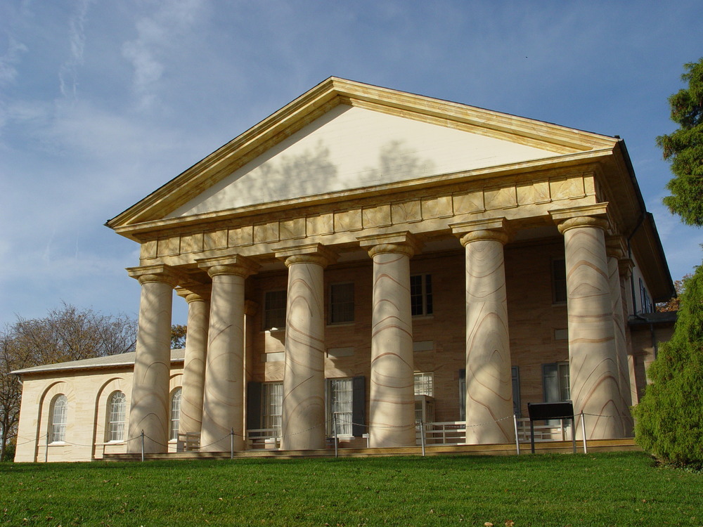 A large stone building with pillars and a manicured lawn on a bright, clear day.