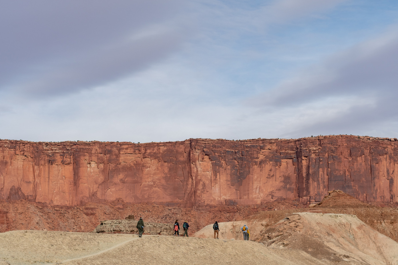 Five people walking along a trail with canyon walls in the background