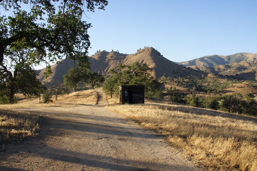 Three rounded peaks can be seen in the distance. Dry grasses and a dirt path in the foreground.