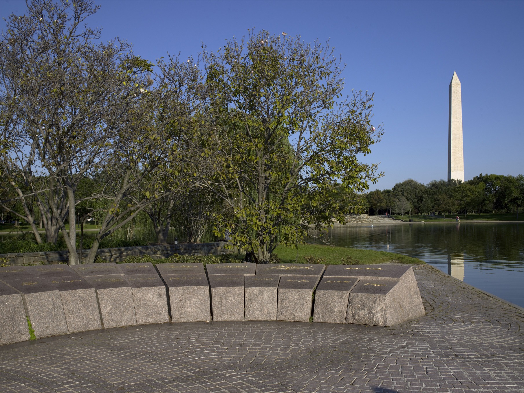 Low stone blocks arranged in an arc of the 56 Signers Memorial with the Washington Monument in the background. 