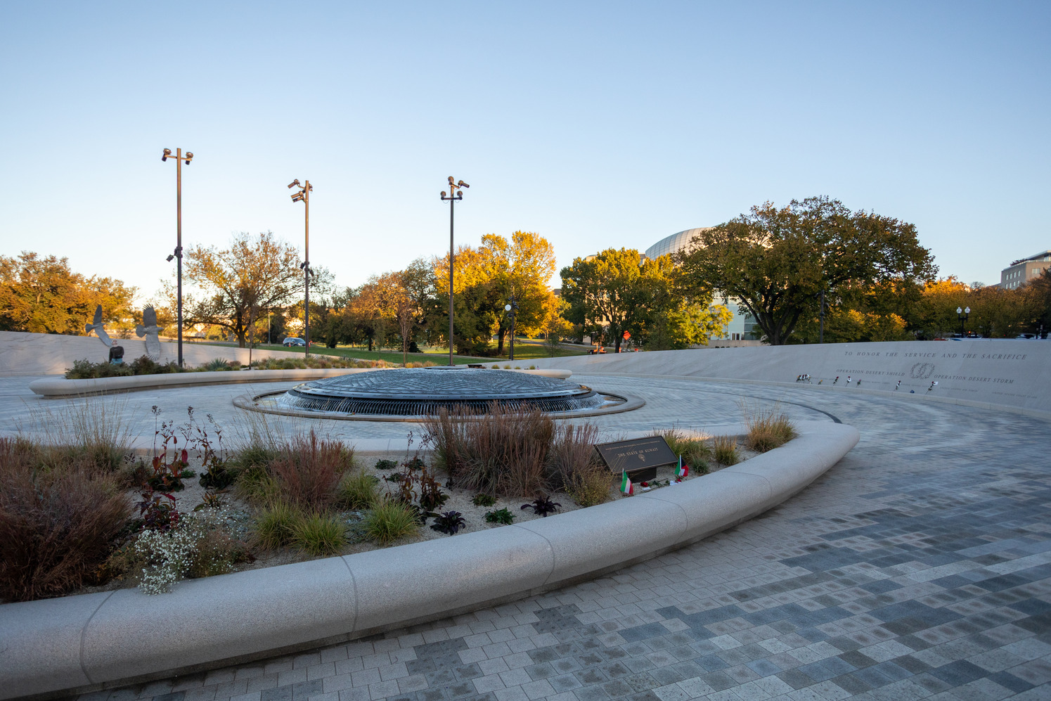 A circular fountain surrounded by landscape beds and encircled by carved and engraved granite walls.