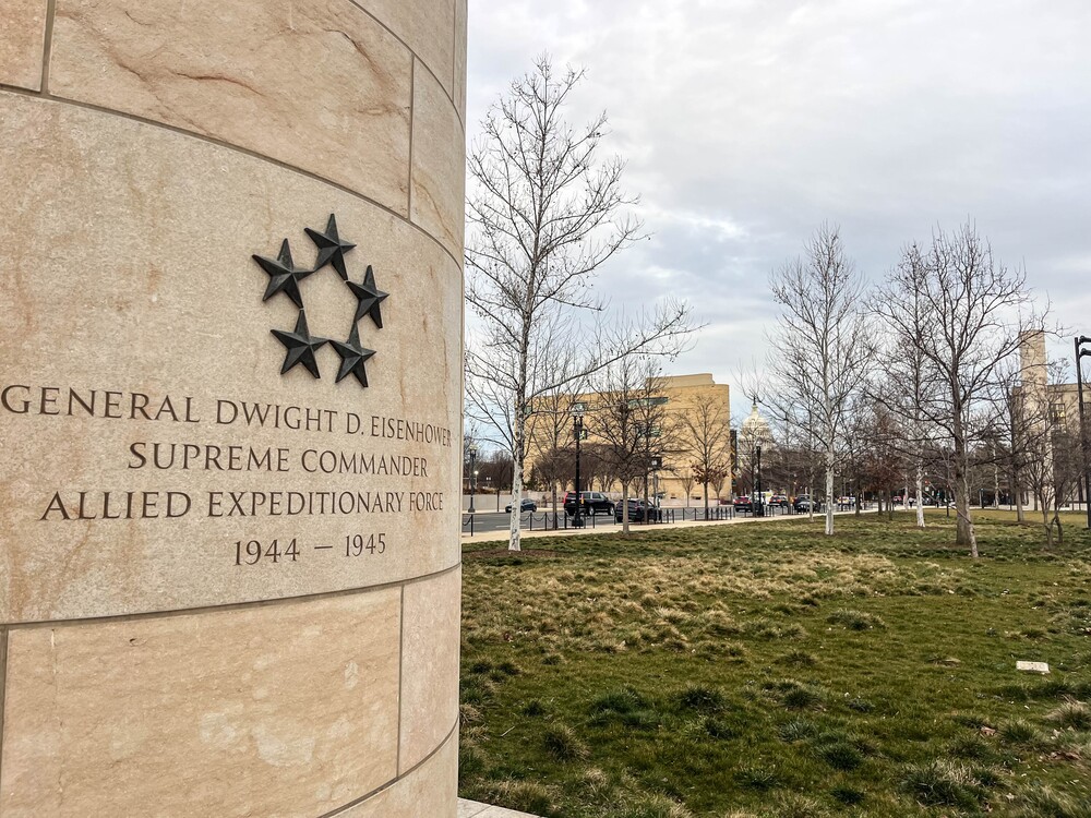 Pillar with five general stars and text reading "General Dwight D. Eisenhower Supreme Commander Allied Expedition Force 1944 - 1945" with the U.S. Capitol building in the distance