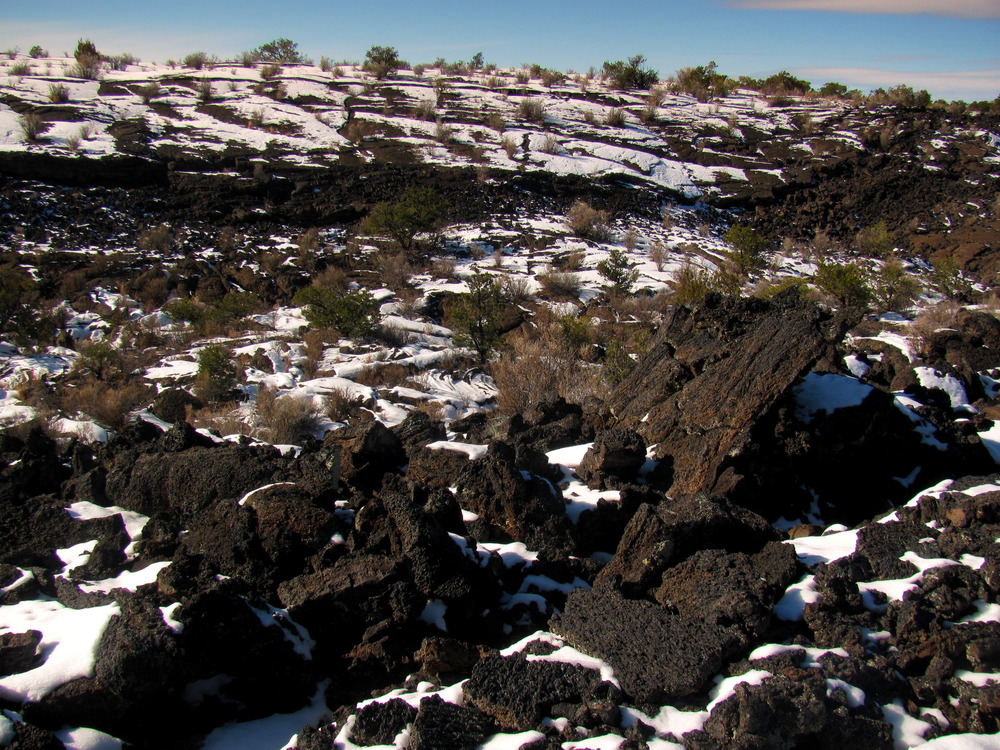 Snow blankets the cracked ridges and craggy rubble.  Green, bushy trees dot the landscape between the exposed rock.