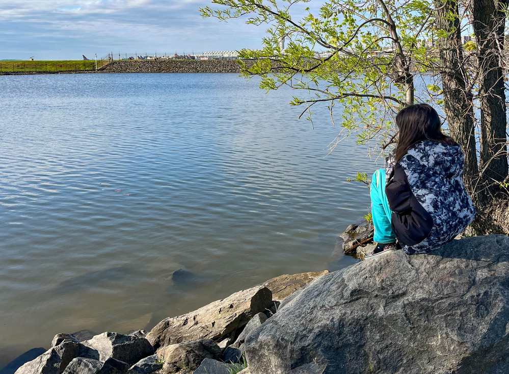 Kid sitting on a rock looking at the river