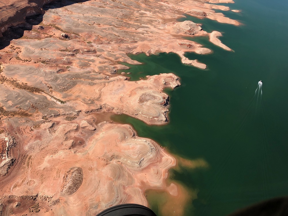 Aerial view of small boat on expanse of shallow water. Sandstone cliffs line the edge of the view.