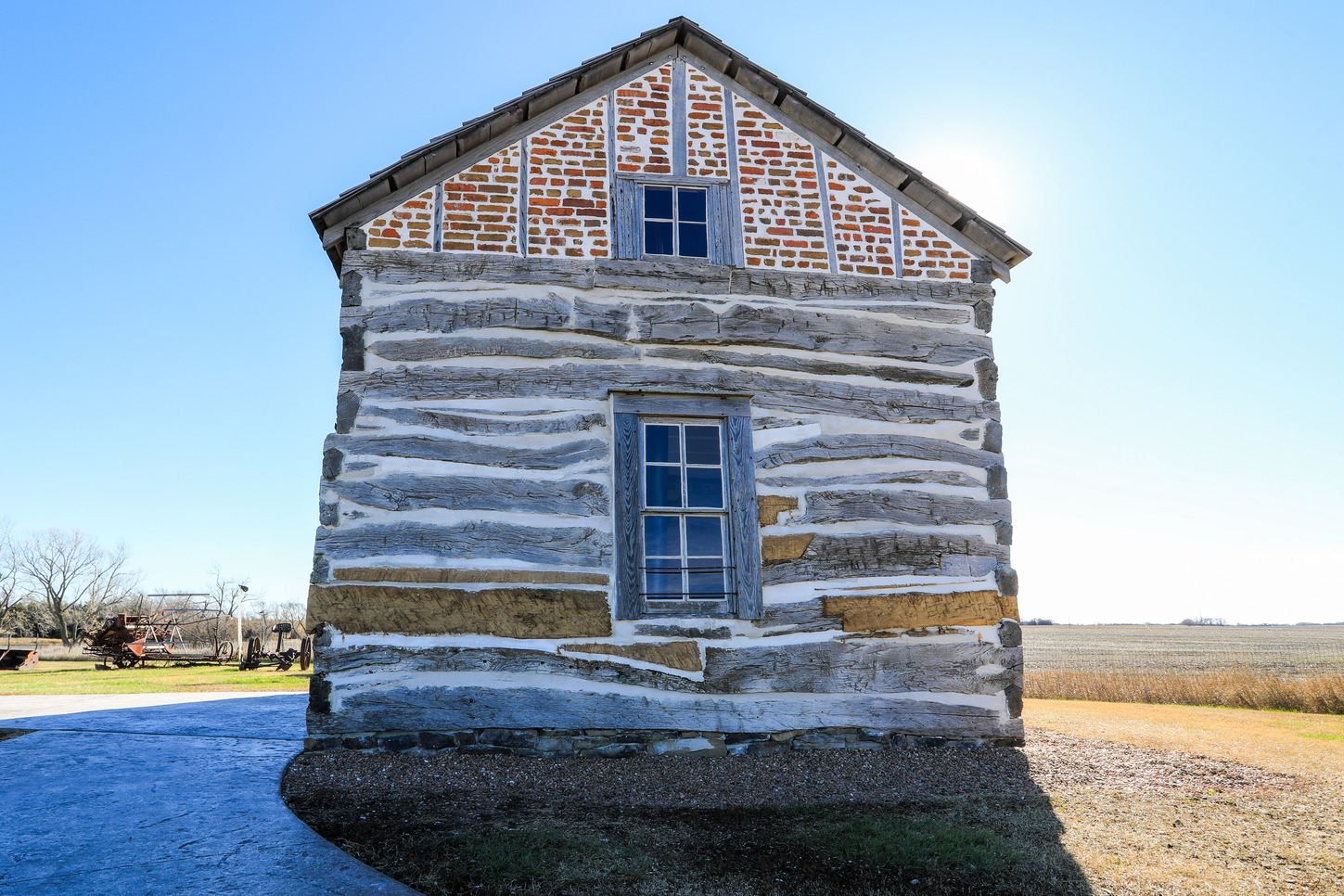 A backlit log cabin displays a patchwork of new and old logs. Older sun-bleached logs are seen contrasting with new brown logs.