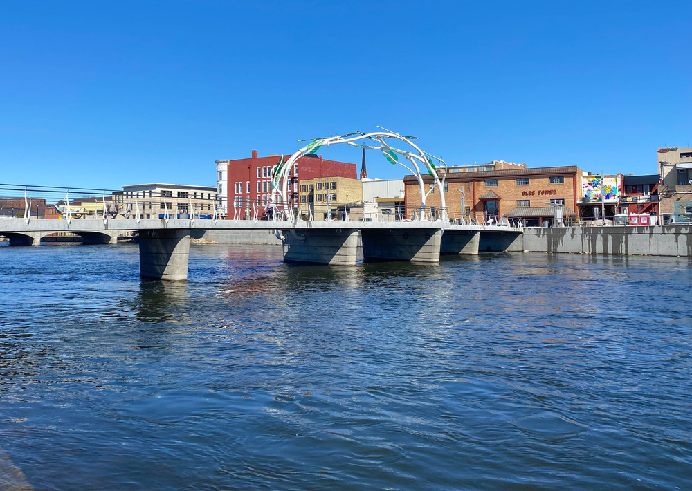 Bridge decorated with a vine sculpture over a river in an urban area