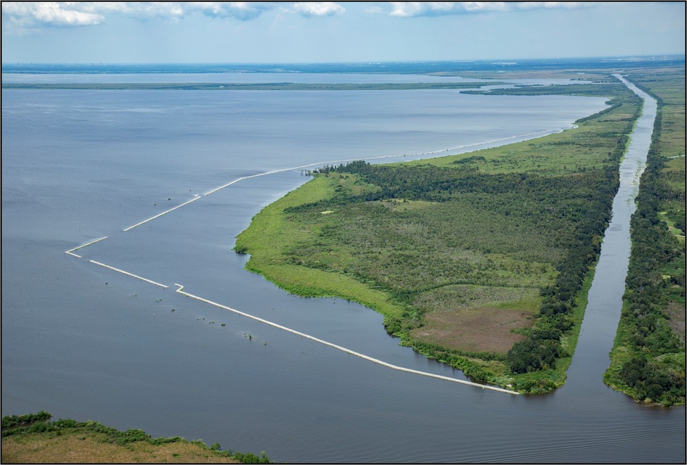 An aerial view of Jean Lafitte National Historic Park and Preserve Shoreline featuring green earth surrounded by a water - a canal on the left side and open water on the right and foreground.