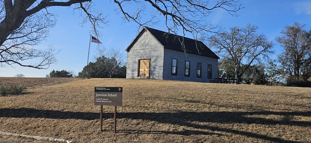 Stone building with wooden door, U.S. flag. Sign reads "Junction School."