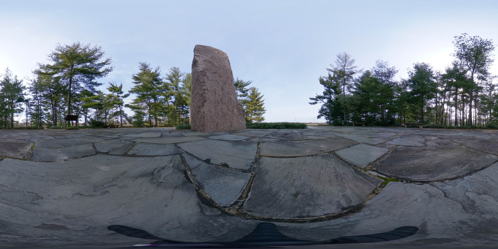 Spherical image of a memorial plaza surrounded by trees. A granite monolith is situated in the center of the plaza. The Washington Monument is in the far distance.
