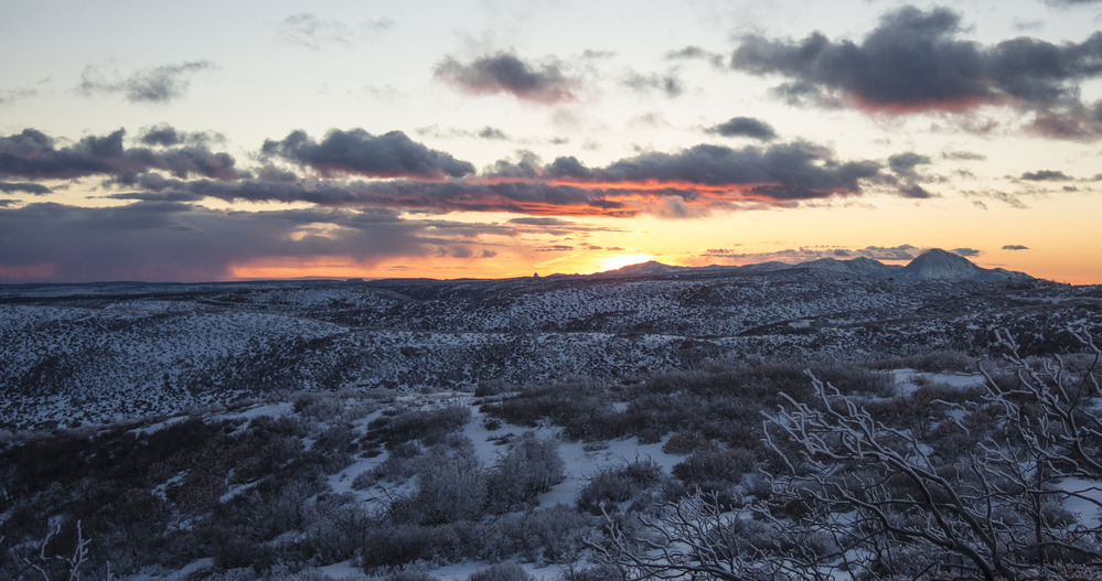 An orange colored sky above a snow covered landscape with snow covered hills in the background.