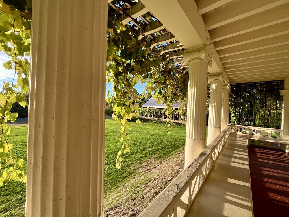 Prominent covered porch with classical Doric columns, overhanging vines, and red floor around sunset