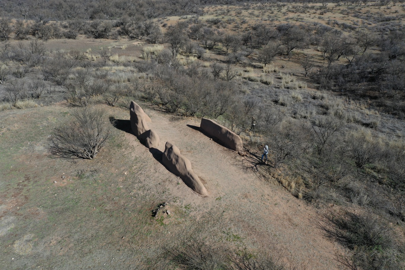 aerial photograph taken from oblique angle, depicts one human figure next to short parallel ruined walls